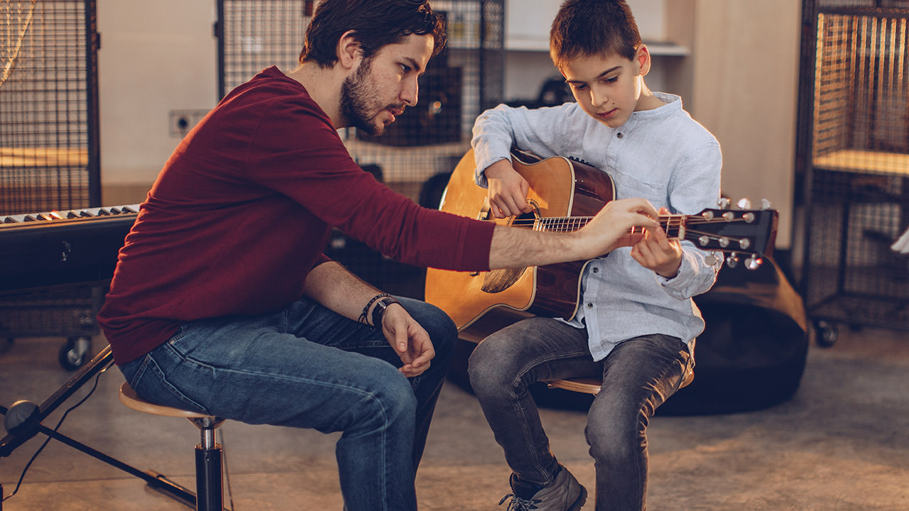 Photo of a guitar teacher giving a lesson to a young boy