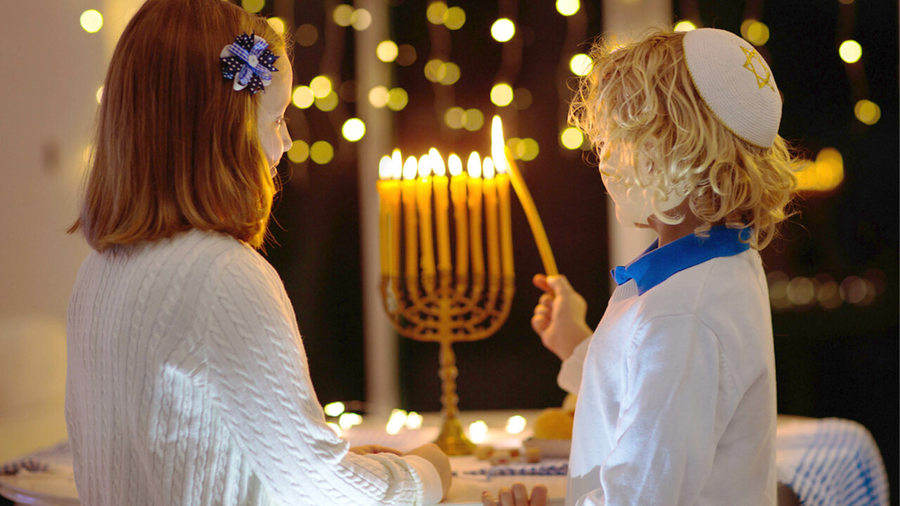 Two young children lighting a candle on a menorah
